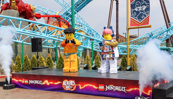 Lego Ninjago characters on stage at Legoland with roller coaster in background.