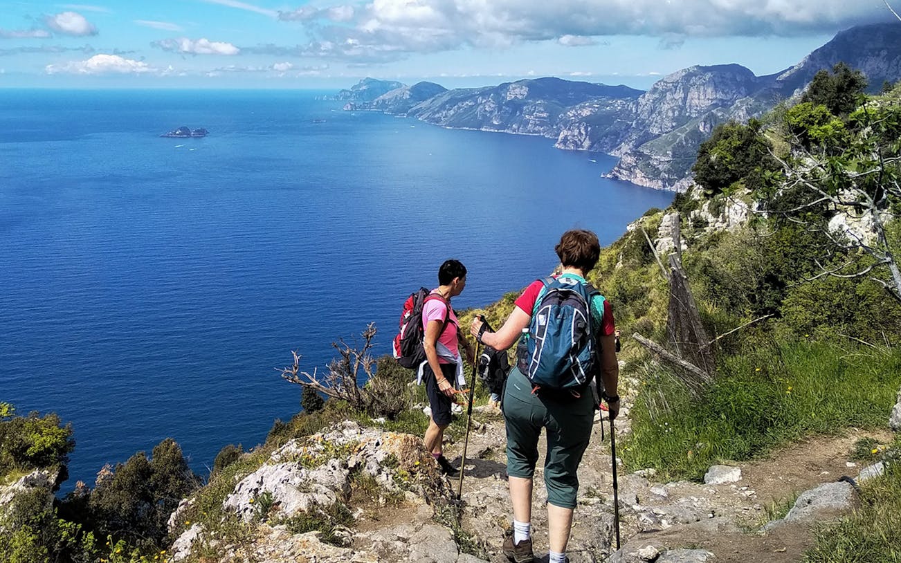 Couple hiking on Path of the Gods, Amalfi Coast, with sea and cliffs in view.