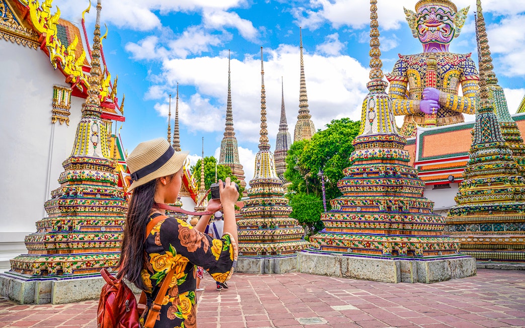 Woman photographing ornate stupas at Wat Pho, Bangkok.