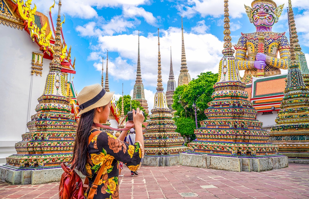 Woman photographing ornate stupas at Wat Pho, Bangkok.
