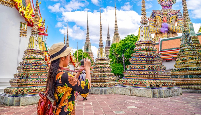Woman photographing ornate stupas at Wat Pho, Bangkok.