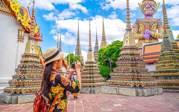 Woman photographing ornate stupas at Wat Pho, Bangkok.