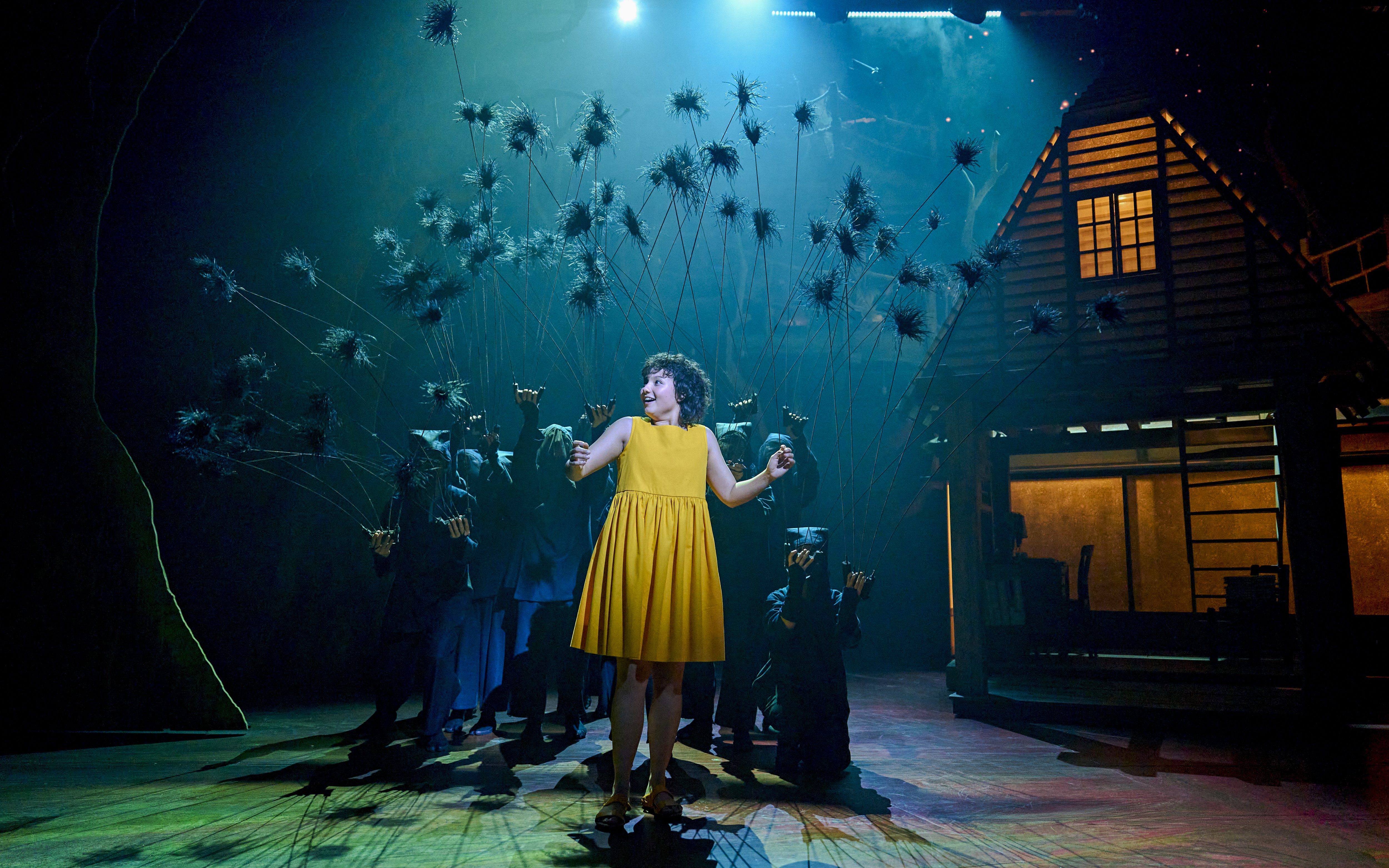 Stage scene from My Neighbour Totoro with a performer in a yellow dress surrounded by puppeteers.