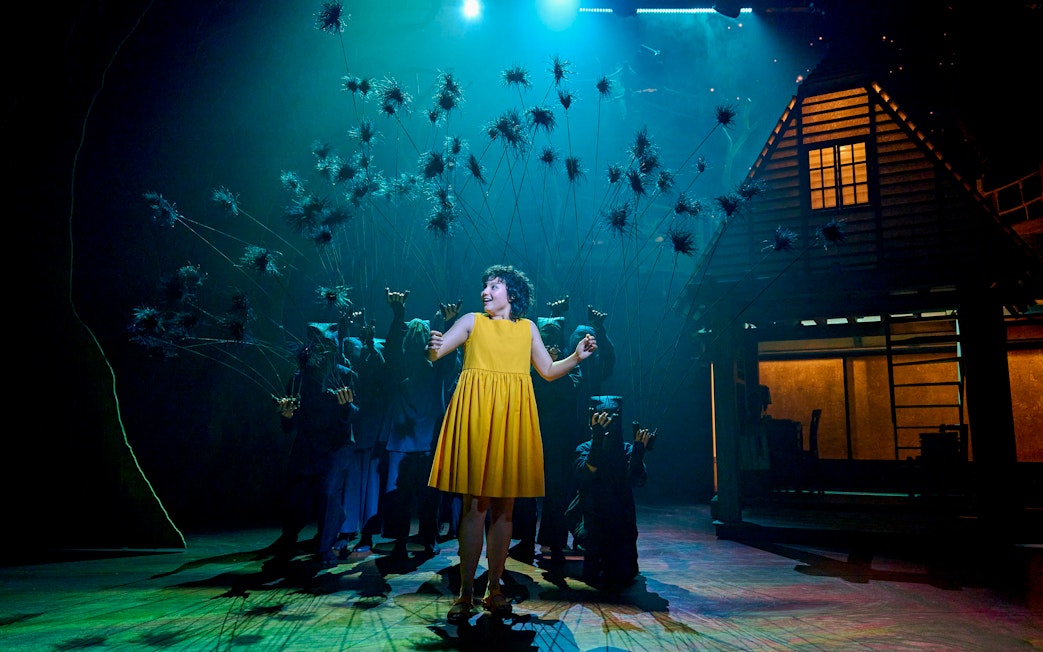 Stage scene from My Neighbour Totoro with a performer in a yellow dress surrounded by puppeteers.