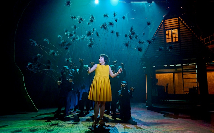 Stage scene from My Neighbour Totoro with a performer in a yellow dress surrounded by puppeteers.