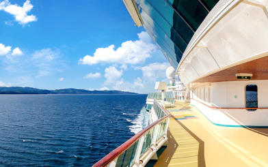 Cruise ship deck overlooking ocean and distant coastline on a sunny day.