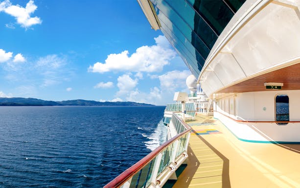 Cruise ship deck overlooking ocean and distant coastline on a sunny day.