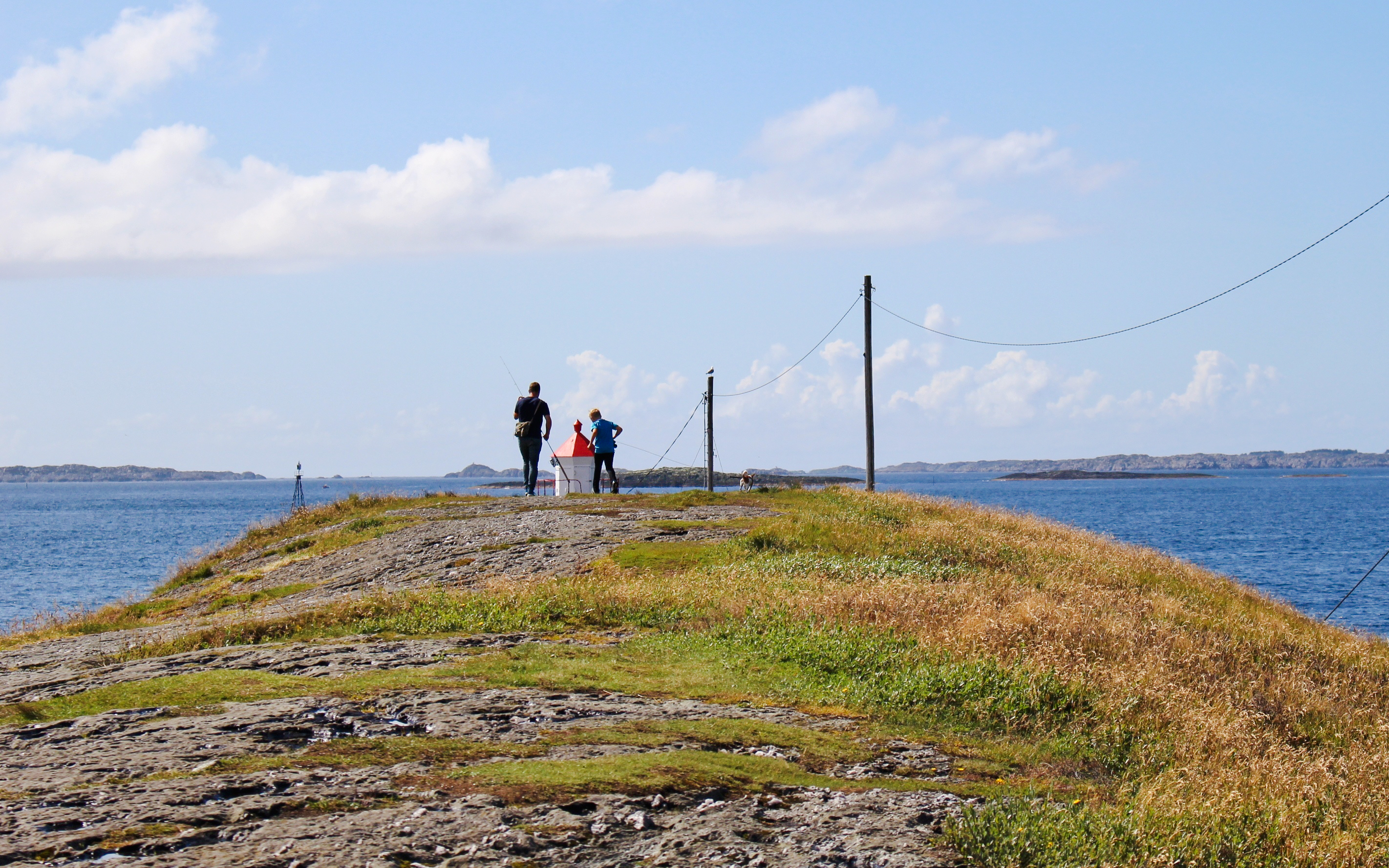 Visitors walking near a lighthouse on a coastal path in Haugesund, Norway.