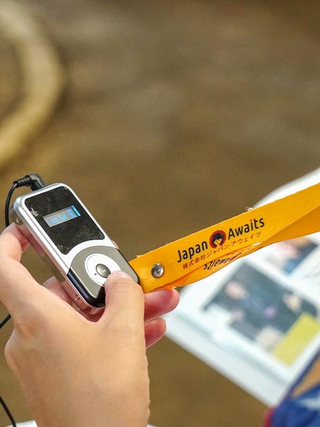 Person holding an audio guide with "Japan Awaits" lanyard during sumo stable tour.