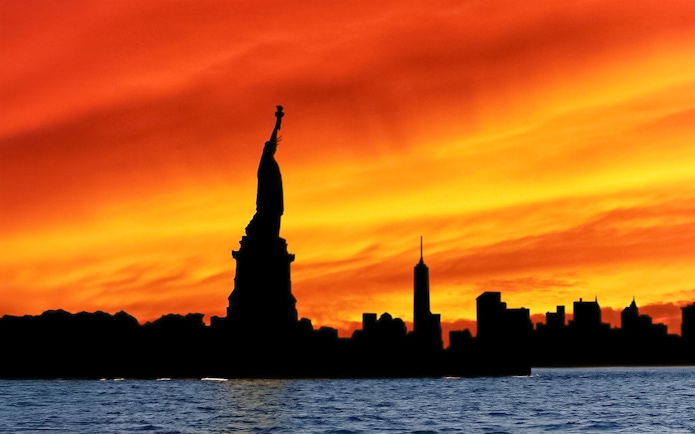 Statue of Liberty silhouette against vibrant sunset during Ellis Island cruise.