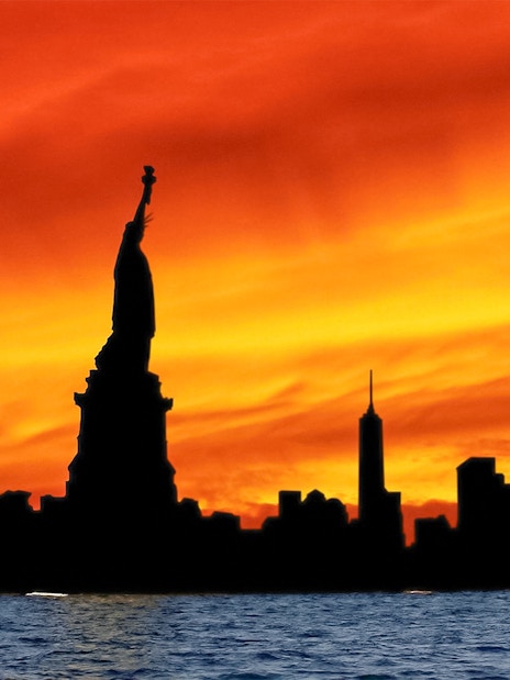Statue of Liberty silhouette against vibrant sunset during Ellis Island cruise.