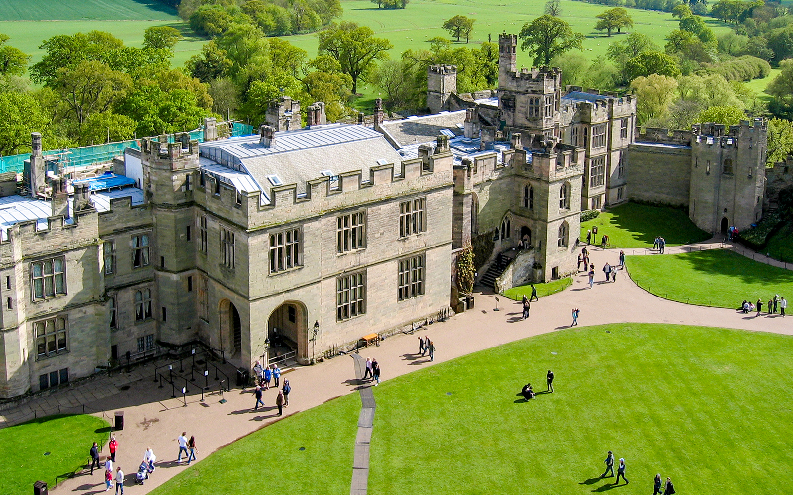 Aerial view of Warwick Castle with visitors walking on the grounds, surrounded by lush greenery.