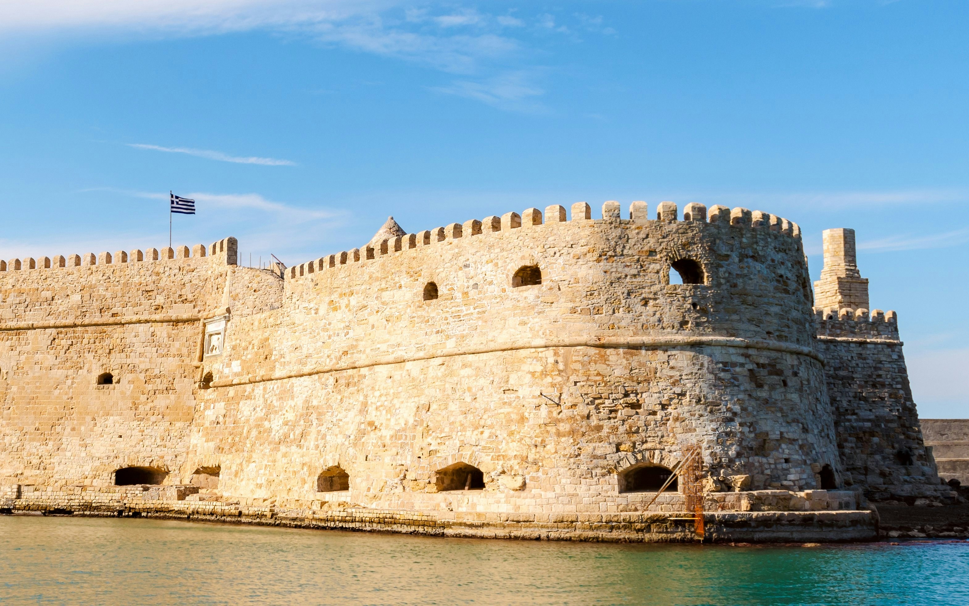Venetian fortress on Crete island, Greece, with Greek flag and stone walls by the sea.