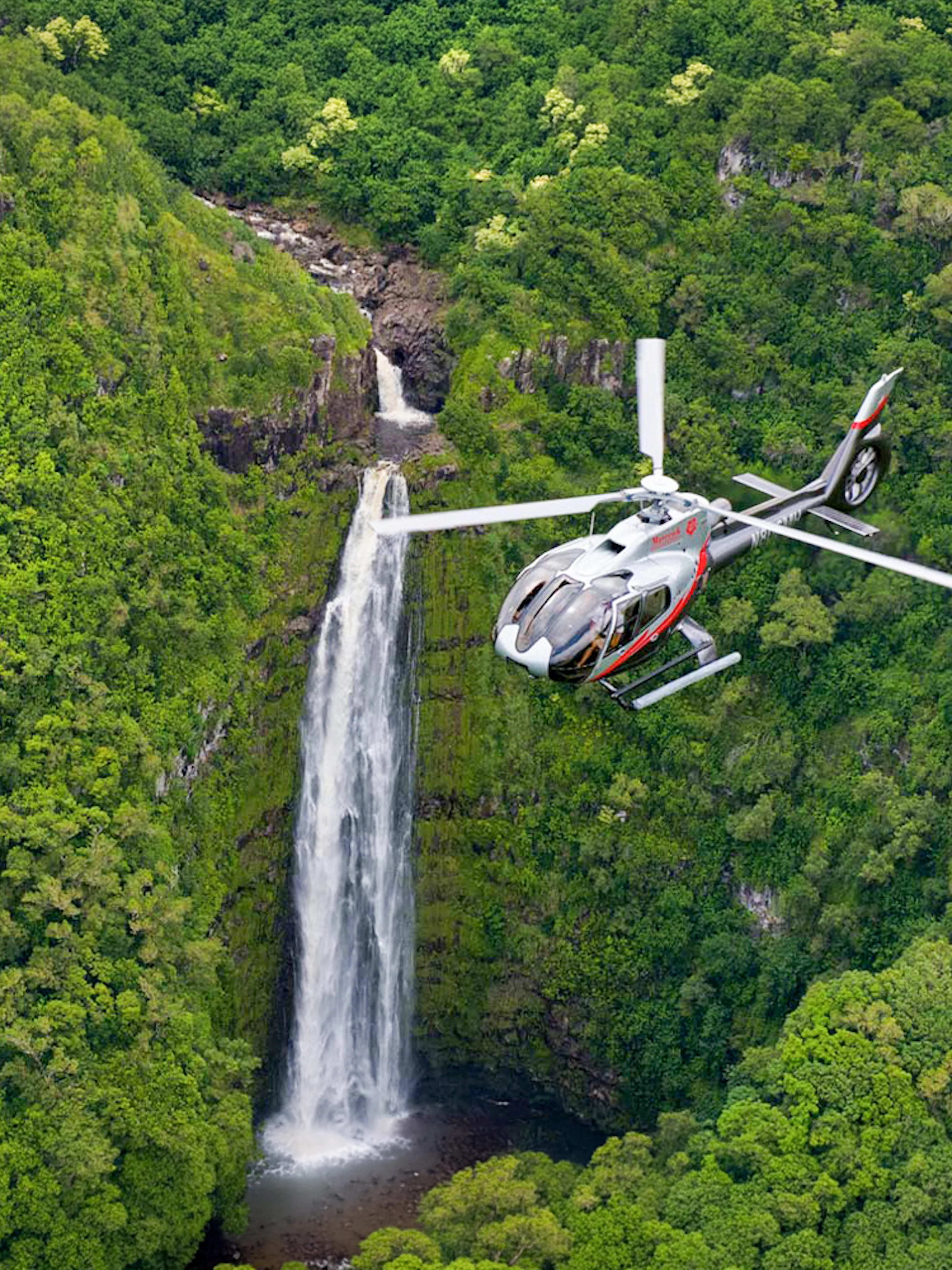 Helicopter flying over lush waterfall in Maui, Hawaii.