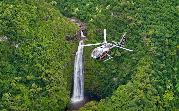 Helicopter flying over lush waterfall in Maui, Hawaii.