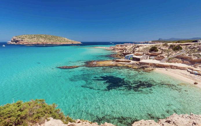 Cala Bassa Beach with clear turquoise water and rocky coastline in Ibiza, Spain.