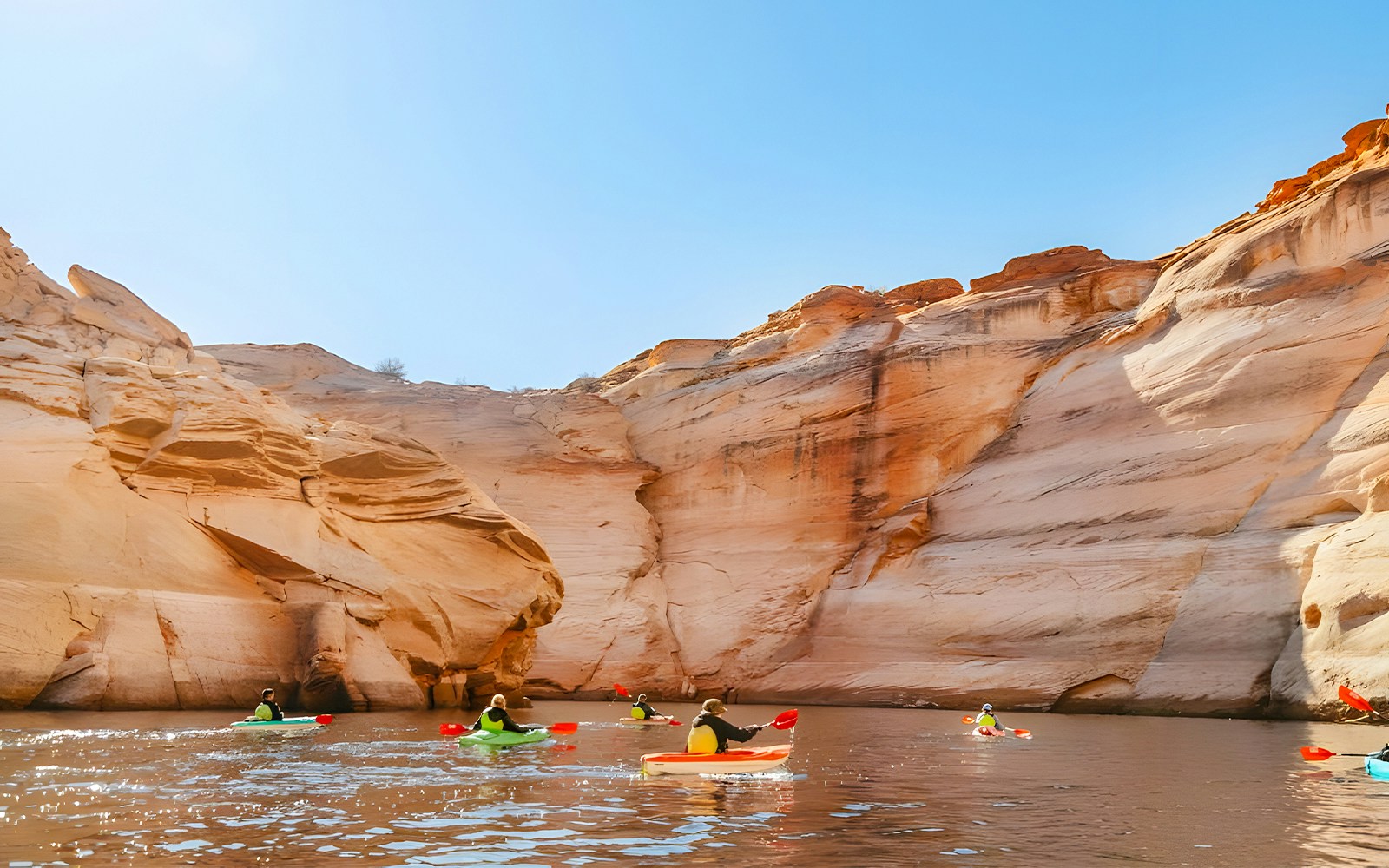 Kayakers paddling on Lake Powell near Antelope Canyon's sandstone cliffs.