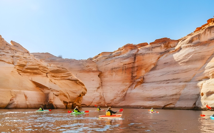 Kayakers paddling on Lake Powell near Antelope Canyon's sandstone cliffs.