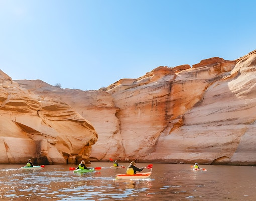Kayakers paddling on Lake Powell near Antelope Canyon's sandstone cliffs.