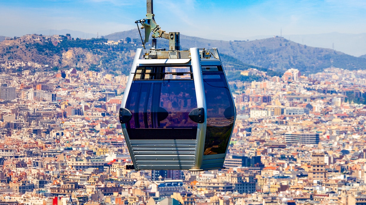 Montjuic Cable Car ascending with panoramic view of Barcelona cityscape.