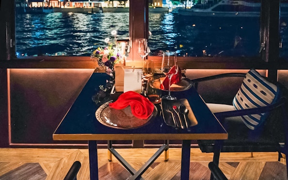 Elegant dining setup on Saffron Luxury Cruise by Banyan Tree with waterfront view.