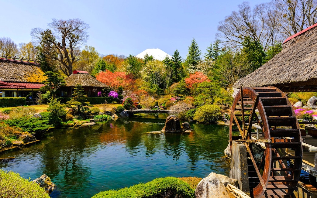 Traditional Japanese garden with waterwheel, vibrant foliage, and Mt. Fuji in the background at Lake Kawaguchiko.