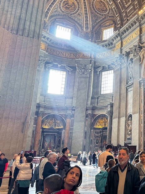 St. Peter's Basilica interior with tourists exploring ornate architecture and sculptures.