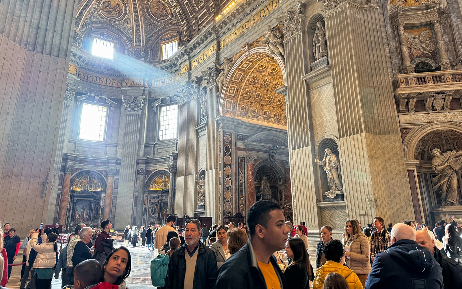 Tourists exploring the interior of St. Peter's Basilica, Vatican City, with ornate architecture and religious art.