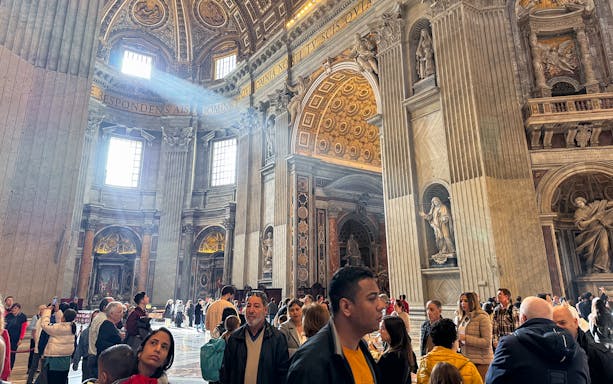 St. Peter's Basilica interior with tourists exploring ornate architecture and sculptures.