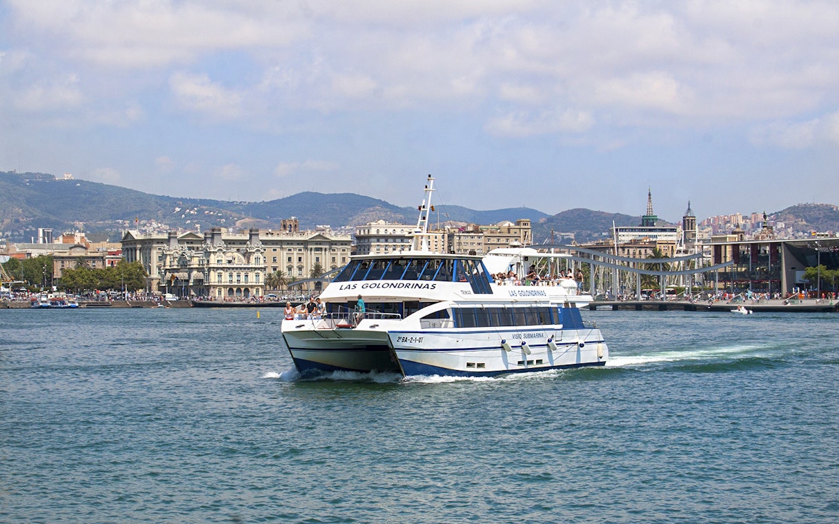 Las Golondrinas boat cruising Barcelona's coastline with city skyline.
