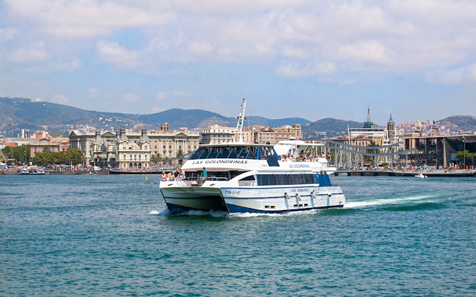 Las Golondrinas boat cruising Barcelona's coastline with city skyline.