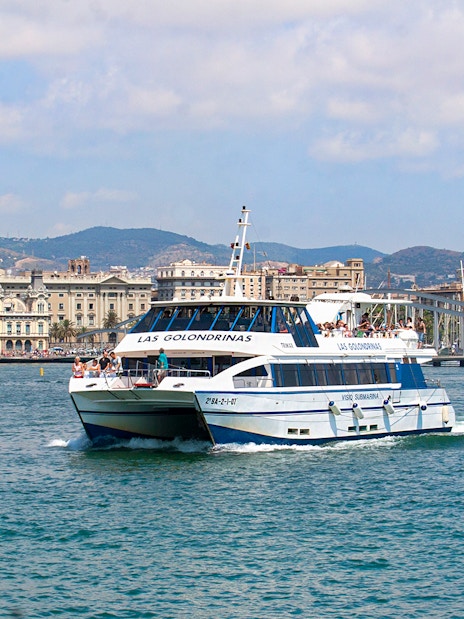Las Golondrinas boat cruising Barcelona's coastline with city skyline.