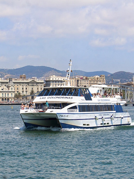 Las Golondrinas boat cruising Barcelona's coastline with city skyline.