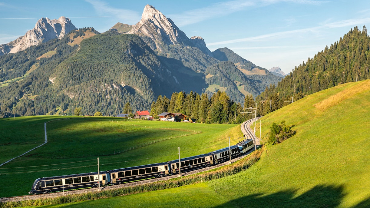 GoldenPass Express train traveling through lush green hills with Interlaken mountains in the background.
