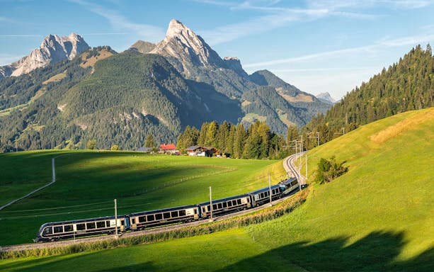 GoldenPass Express train traveling through lush green hills with Interlaken mountains in the background.