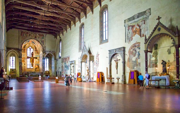 Interior of Basilica of San Francesco in Arezzo, Italy, featuring frescoes and visitors exploring.