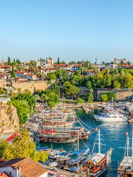 Old harbor with boats in Antalya, Turkey, surrounded by historic buildings and lush greenery.