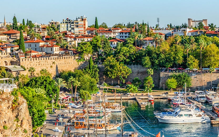 Old harbor with boats in Antalya, Turkey, surrounded by historic buildings and lush greenery.