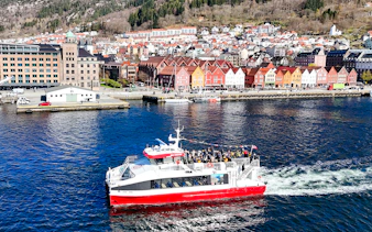 Cruise boat on Mostraumen fjord with Bergen's colorful waterfront buildings in view.