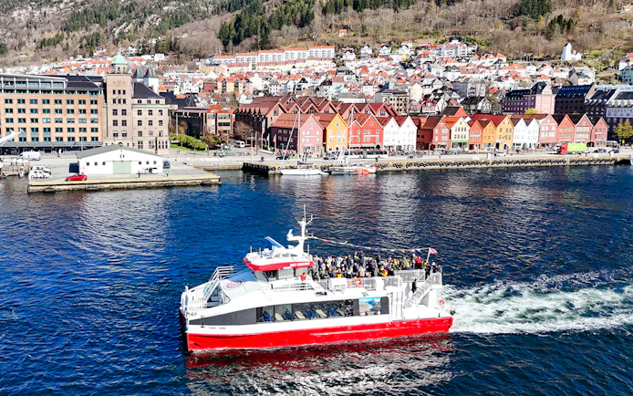 Cruise boat on Mostraumen fjord with Bergen's colorful waterfront buildings in view.