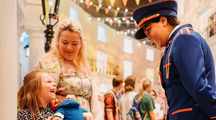 Child holding Paddington Bear toy, smiling with adult and costumed guide at Paddington Bear Experience.