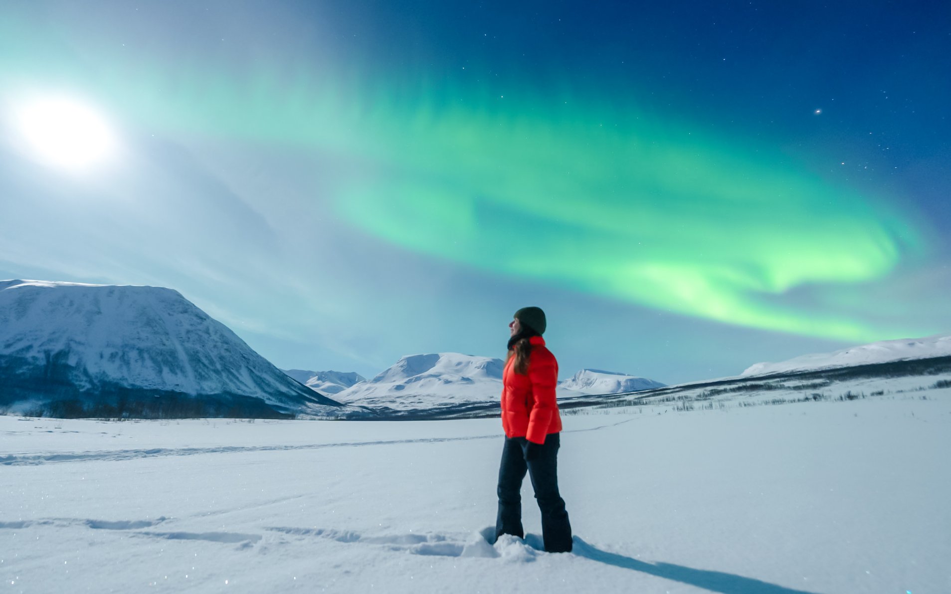 Woman observing Northern Lights in Tromso, Norway with snowy mountains in the background.