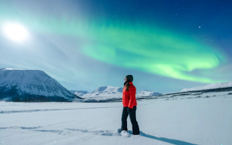 Woman observing Northern Lights in Tromso, Norway with snowy mountains in the background.