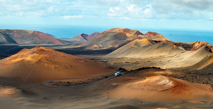 Timanfaya National Park volcanic landscape with winding road and distant ocean view.