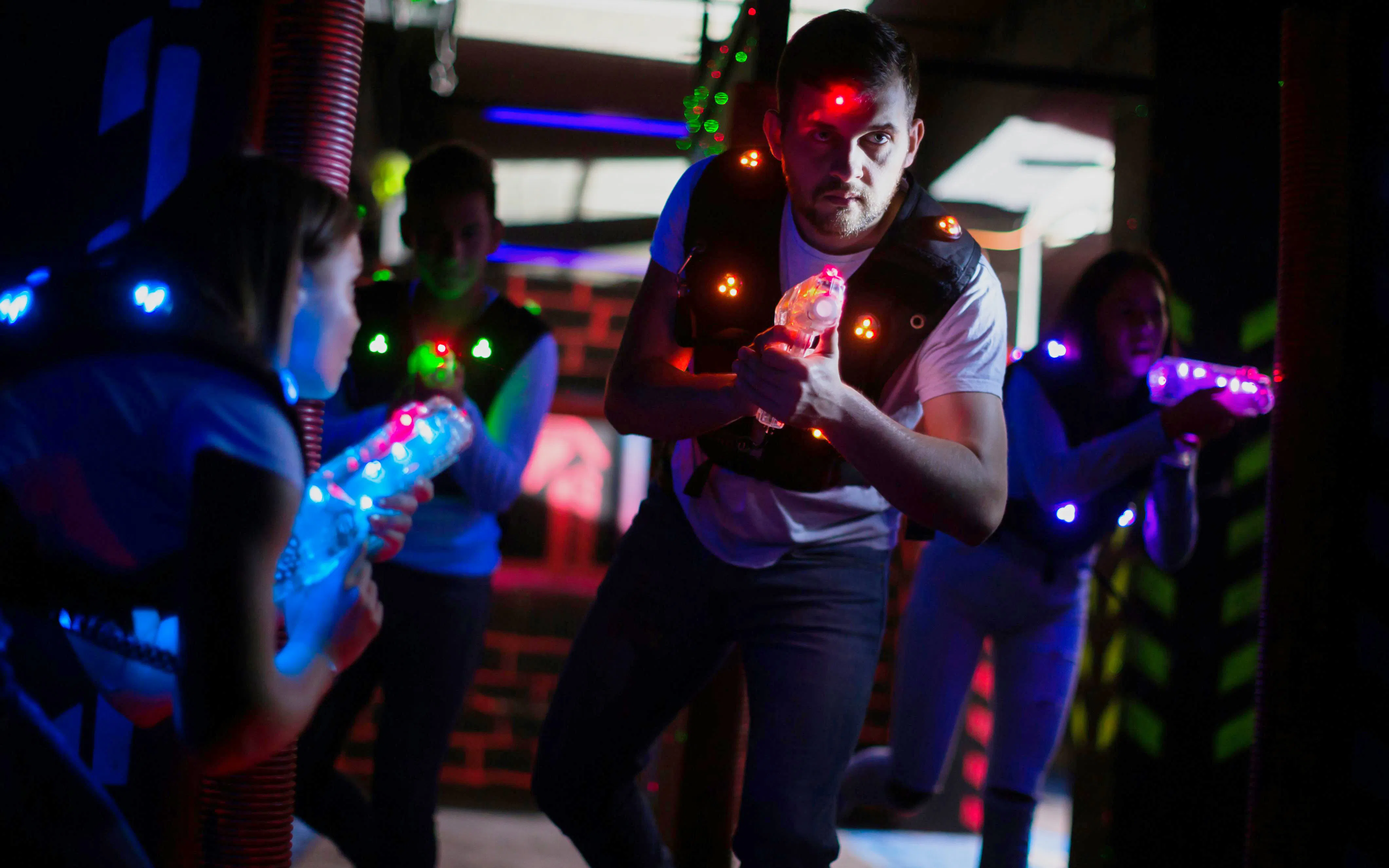 Visitors engaging in a lasertag game with glowing vests and laser guns.
