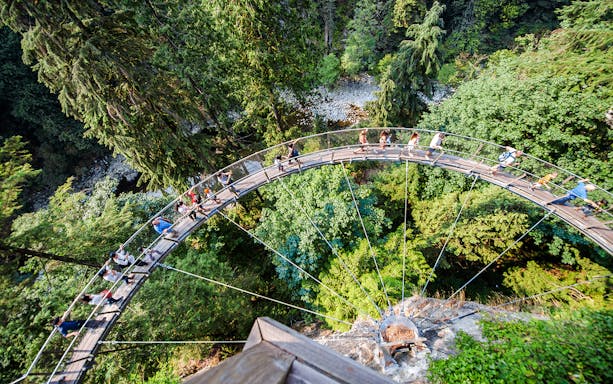 Visitors walking on Capilano Suspension Bridge in Vancouver, surrounded by lush forest.
