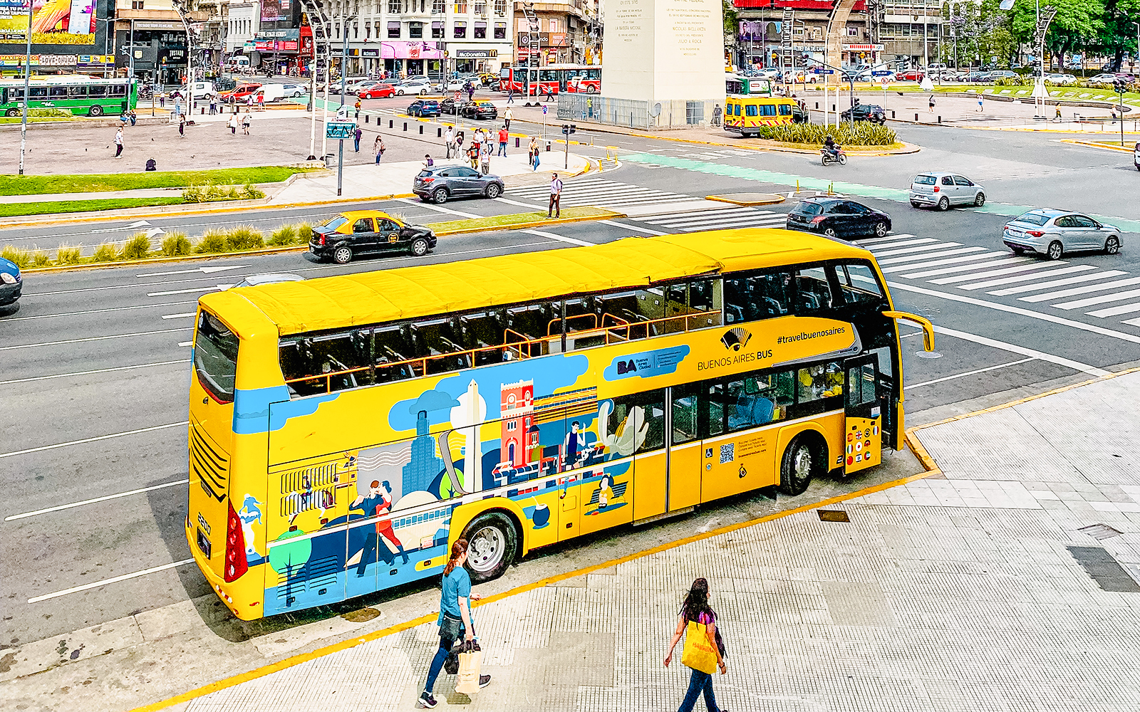 Yellow Buenos Aires tour bus near the Obelisk in a busy city street.