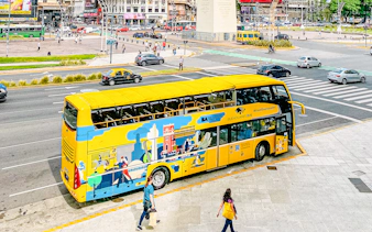 Yellow Buenos Aires tour bus near the Obelisk in a busy city street.