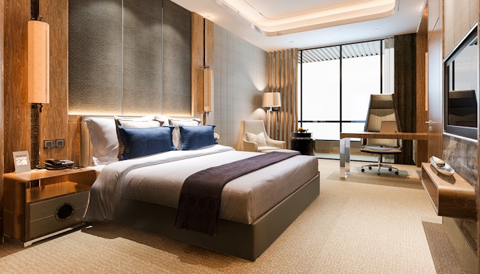 Luxury modern bedroom suite with king bed, desk, and large window in hotel.