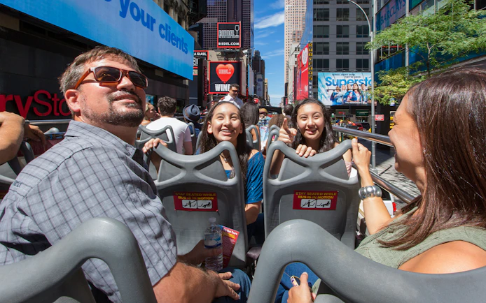 Passengers enjoying Big Bus New York tour with Empire State Building in background.